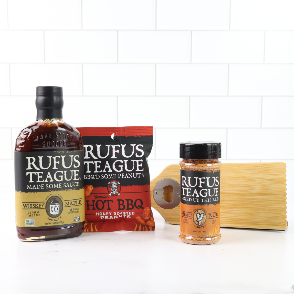 Three bottles of Rufus Teague sauce and a bag of peanuts on a white tiled background