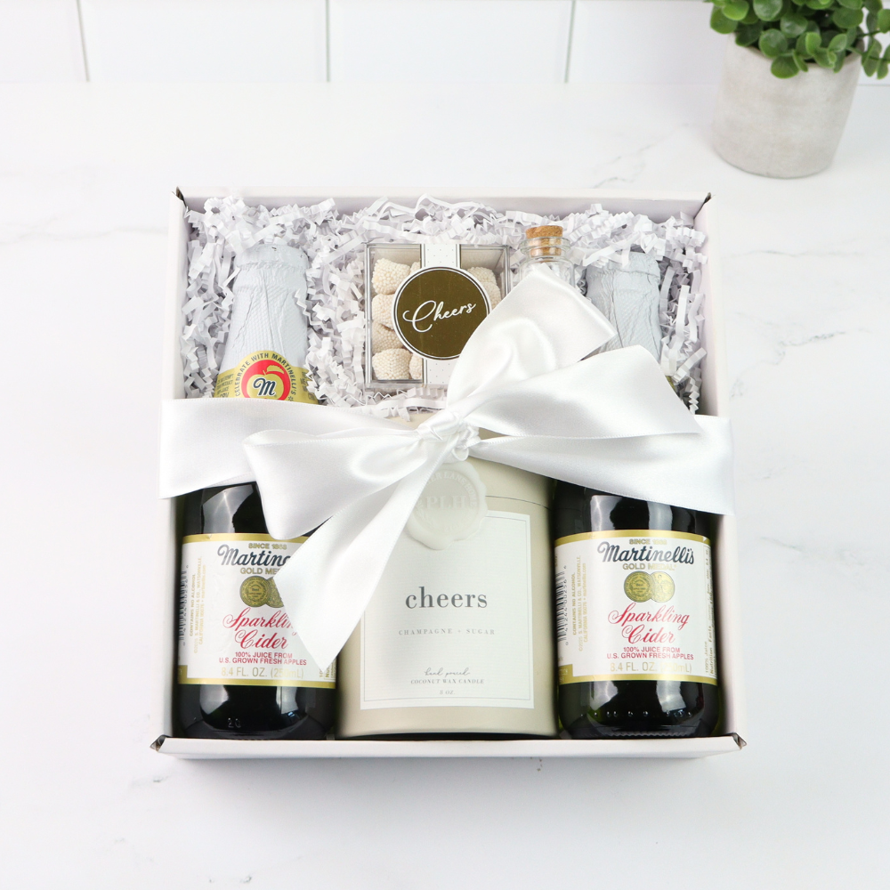 Gift set with Martinelli's sparkling cider and 'Cheers' wine in a box on a white surface.