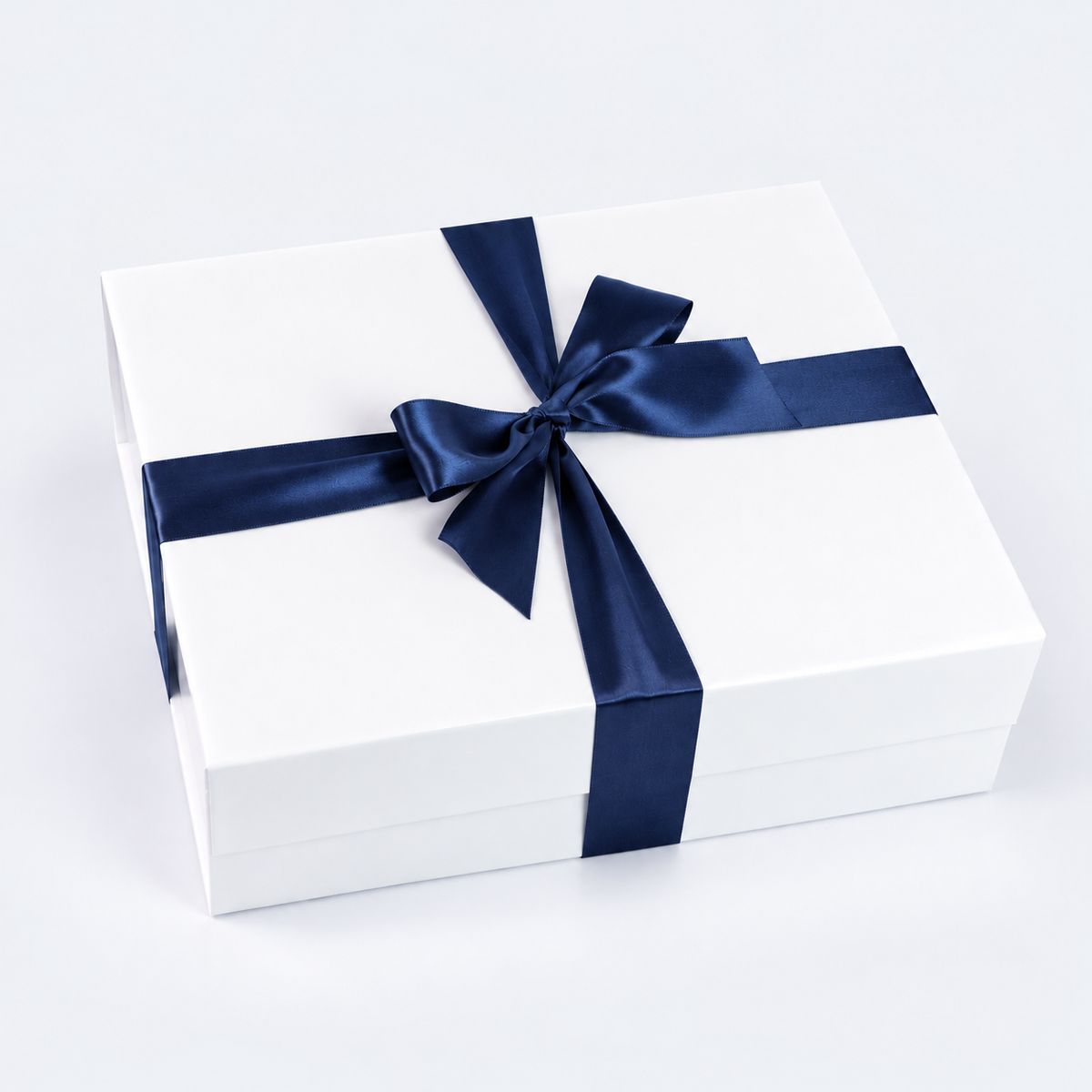 A white rectangular gift box tied with a wide navy blue satin ribbon and bow, photographed on a clean white background.