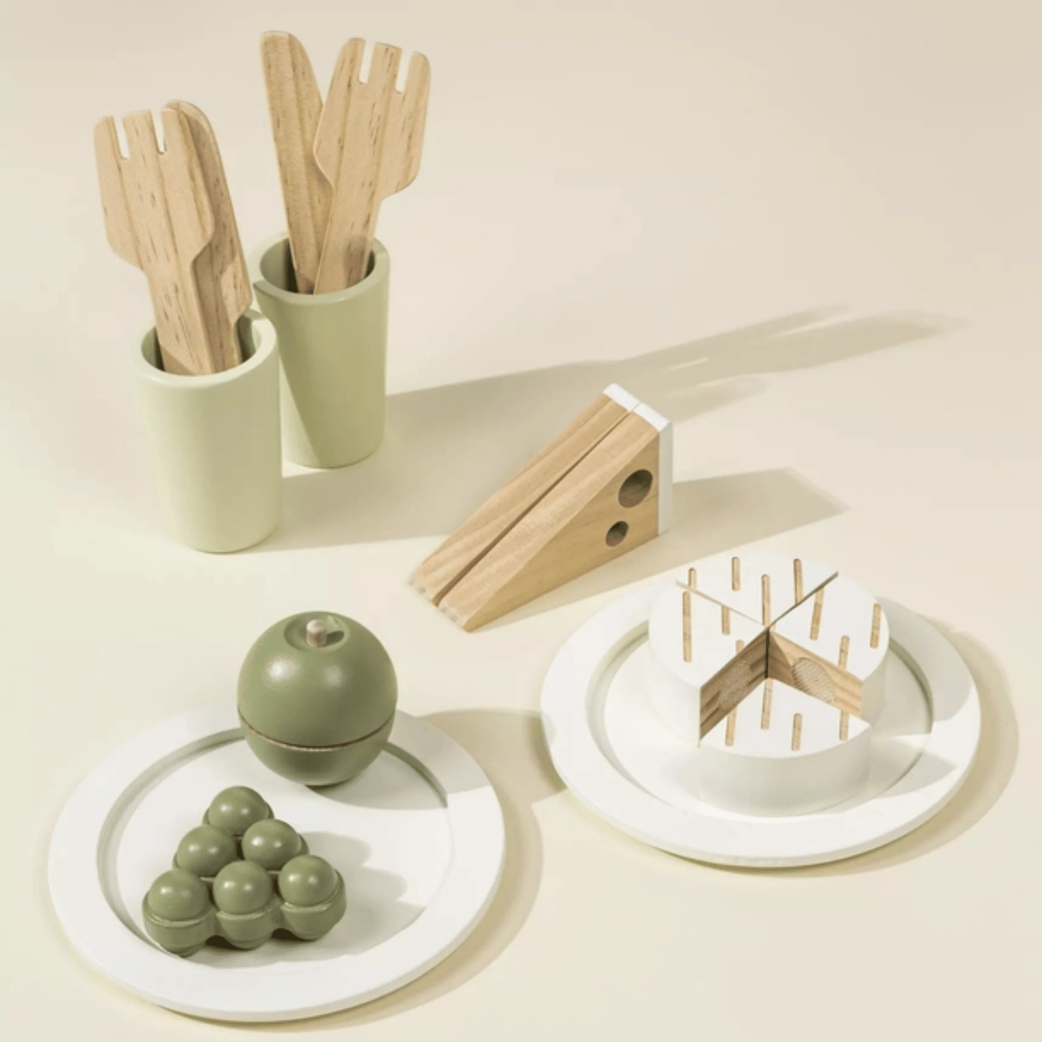Wooden pretend play food including grapes, apple, bread slices, and utensils set on small plates.