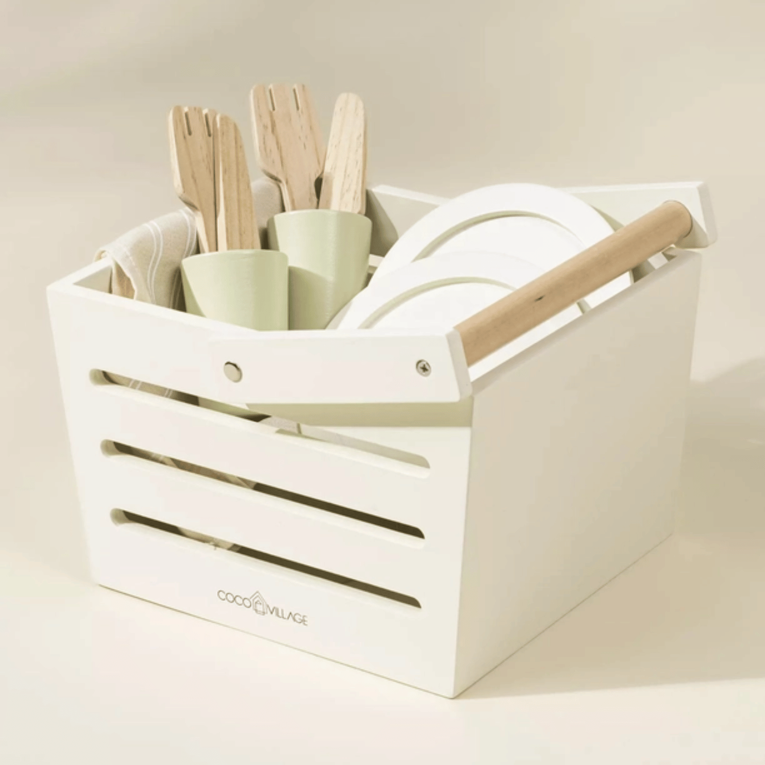 Wooden picnic basket filled with play dishes, cups, utensils, and food pieces in soft neutral colors.