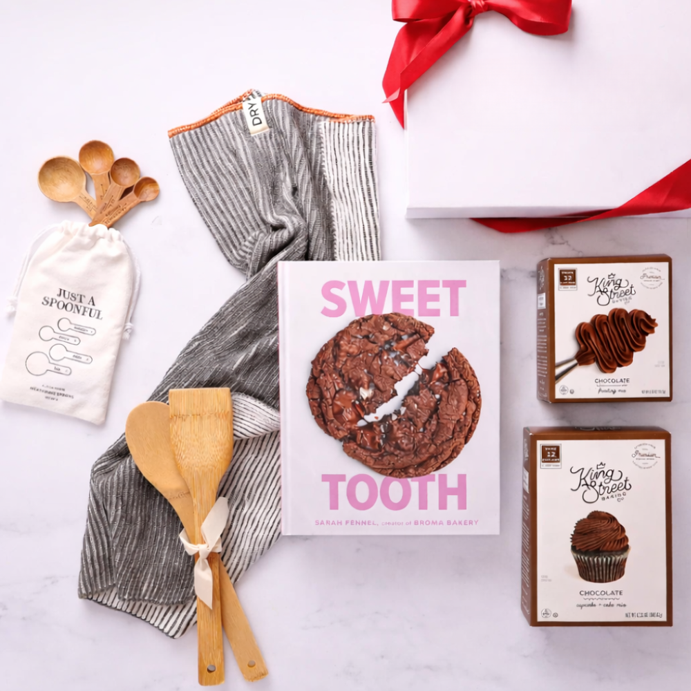Baking-themed gift set with chocolate products, kitchen tools, and a decorative towel on a white background.