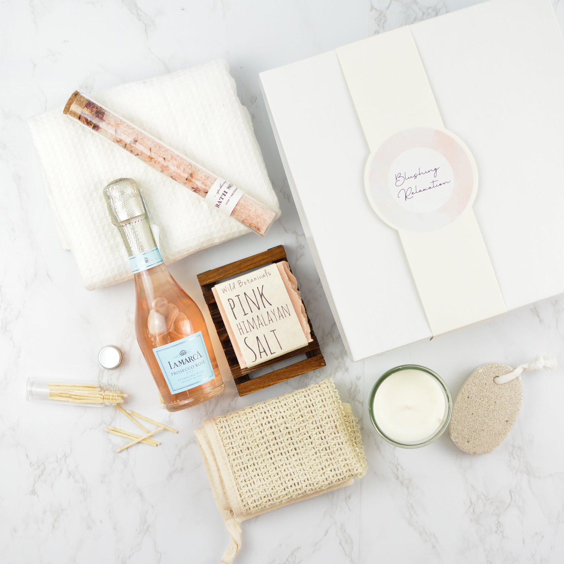 Blushing Relaxation Gift Box with rosé bubbles, bath salts, candle, towel, and spa accessories arranged in a white gift box