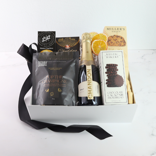 Gift basket with Chandon champagne, snacks, and a card on a white background