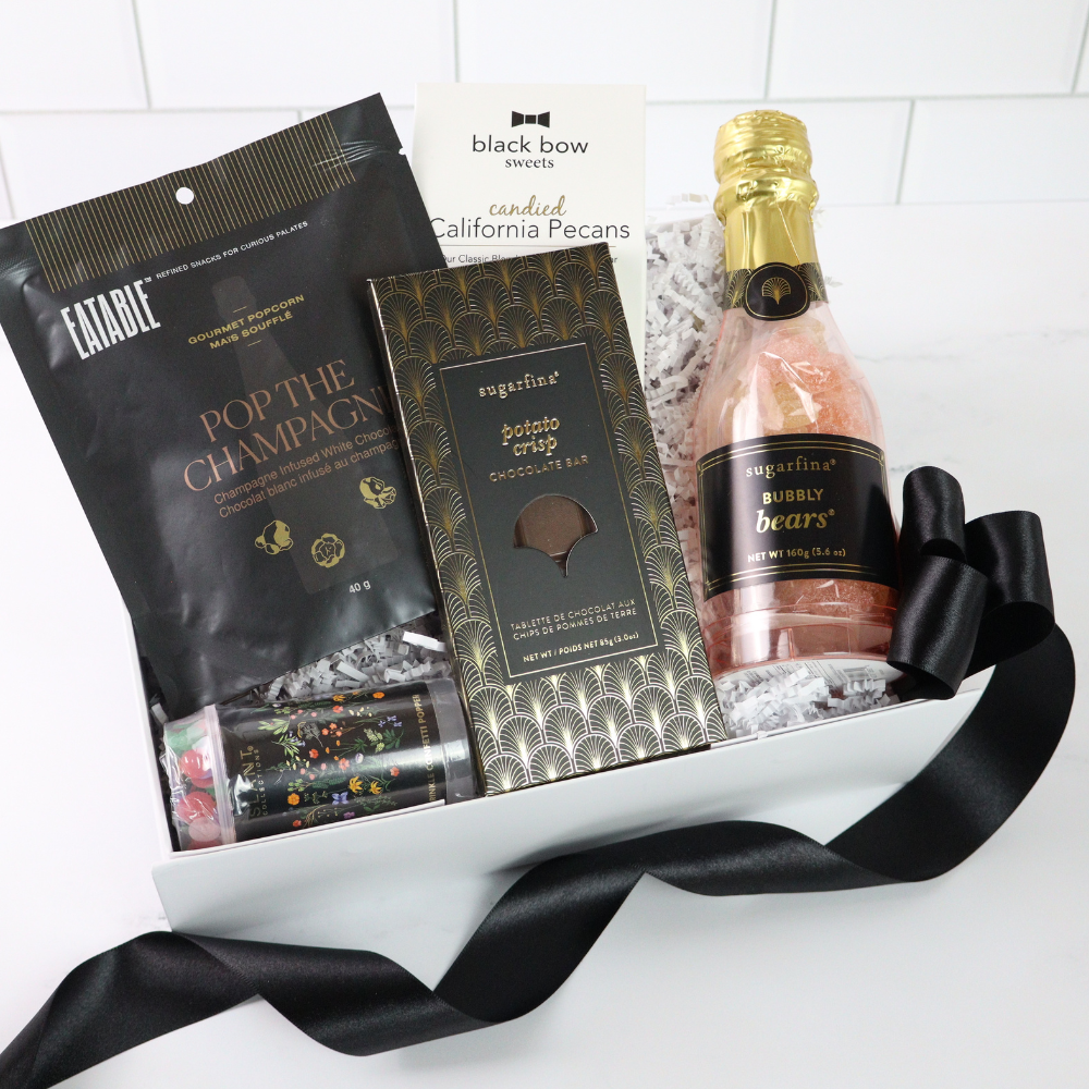 Gift basket with chocolate bar, champagne, and other treats on a white background