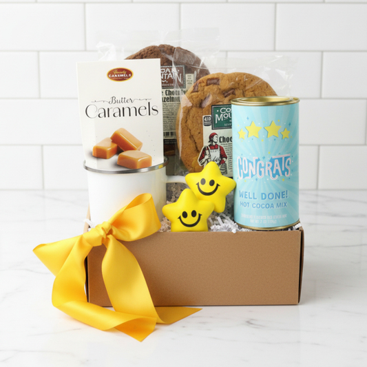 Gift box with 'Butter Caramels', 'congrats', and 'Well Done!' cocoa mix on a white tiled background
