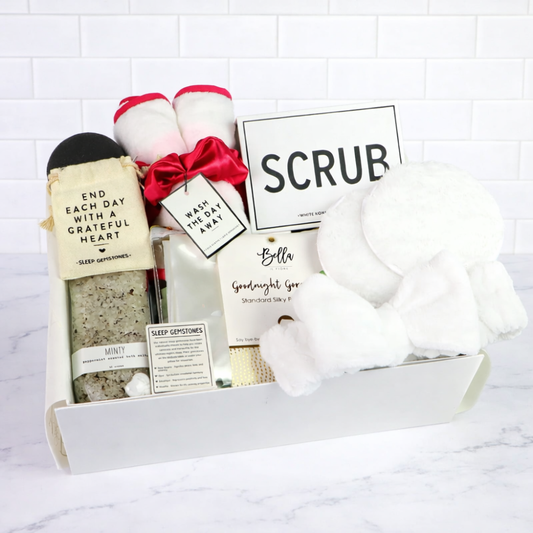 Gift box with bath products including a scrub, soap, and towels on a white background
