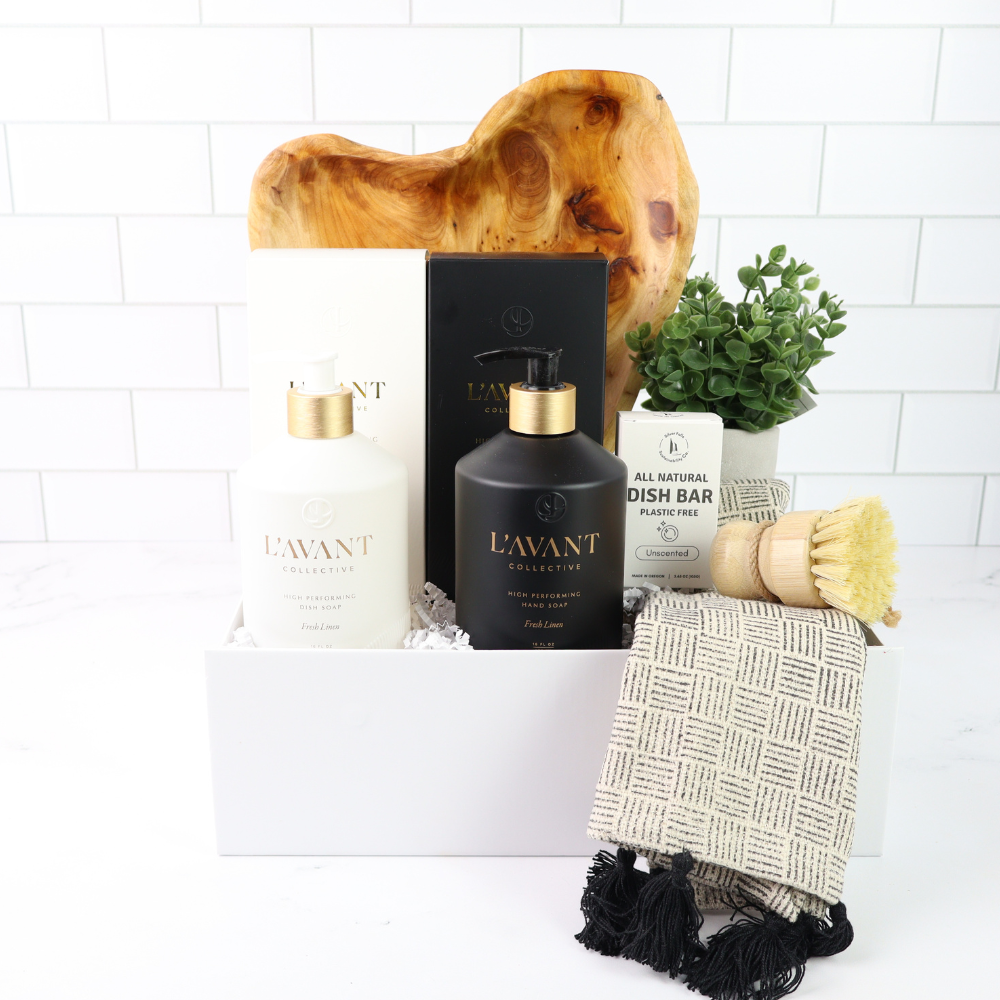 Collection of L'AVANT products including a bottle, candle, and soap on a white surface with a wooden block and plant in the background.