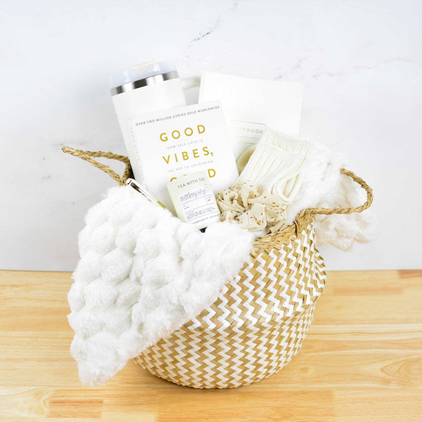 Executive relaxation gift basket with inspirational book, cozy throw blanket, travel tumbler, socks, and self-care accessories arranged in a woven basket