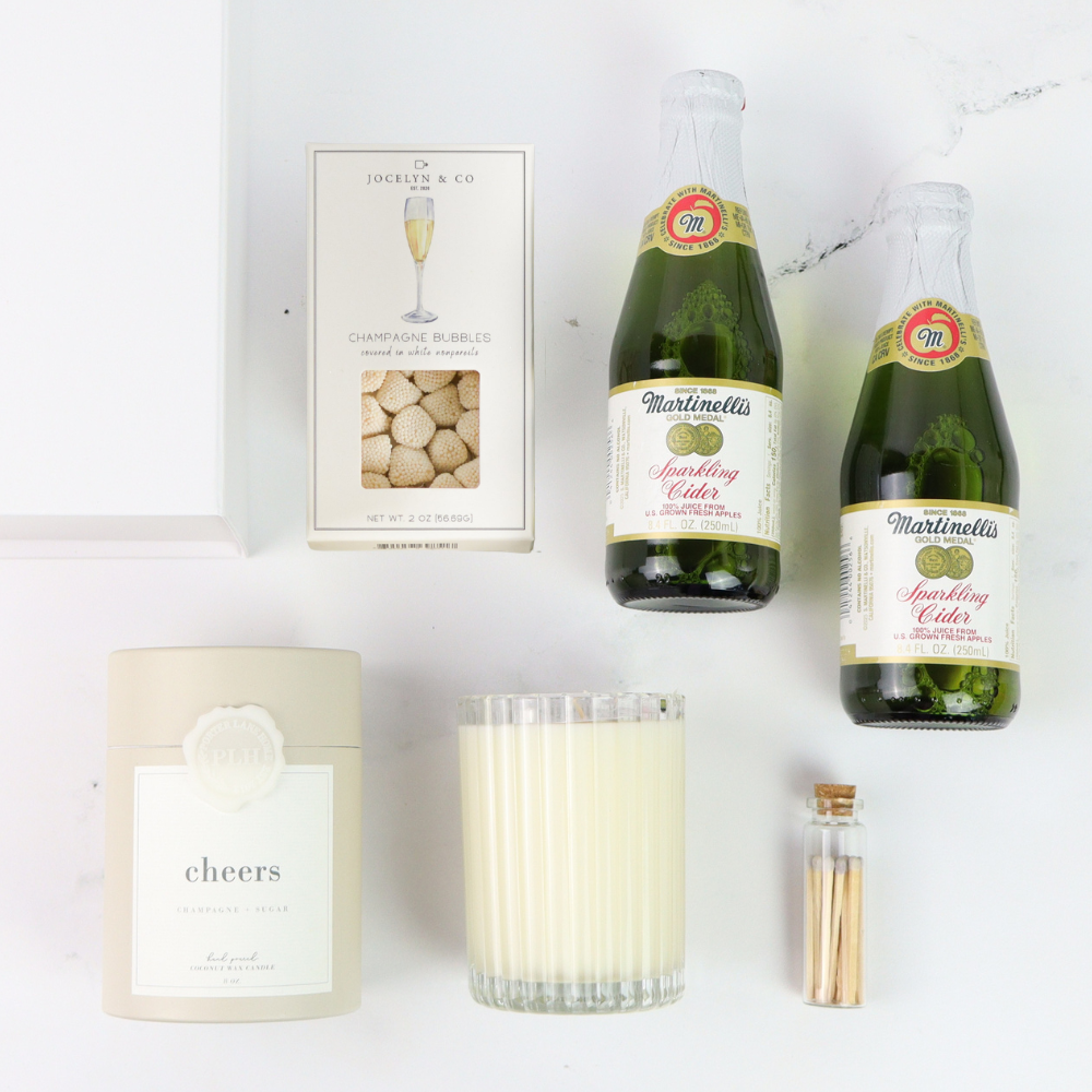 Two bottles of Martinellis sparkling cider, a candle labeled 'cheers', and a box of corks on a white background.