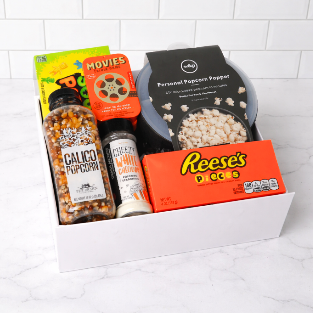 Snack box with popcorn kernels, popcorn flavorings, and Reese's Pieces on a white background