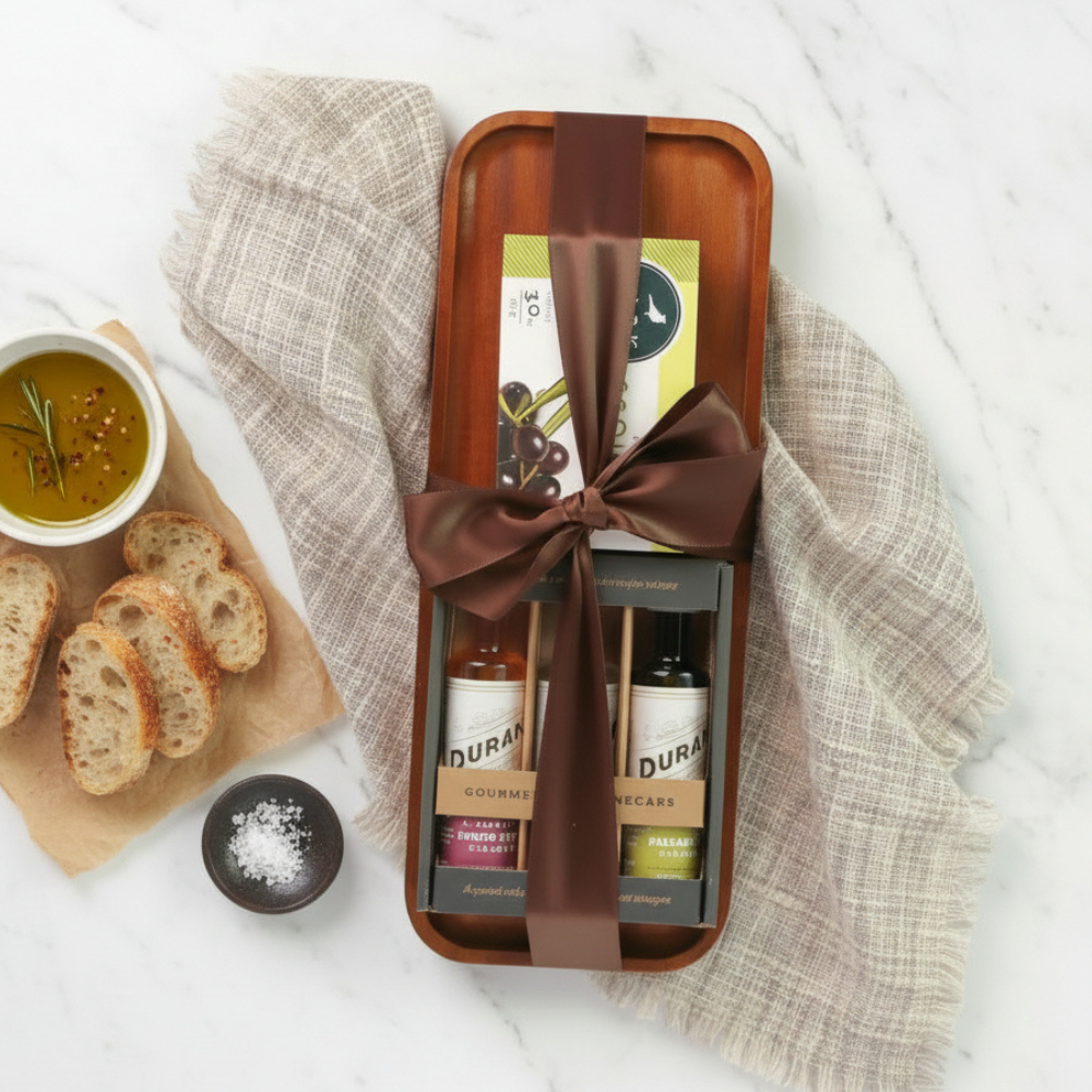 Gift set with olive oil on a wooden tray with a brown ribbon, surrounded by bread and olive oil.