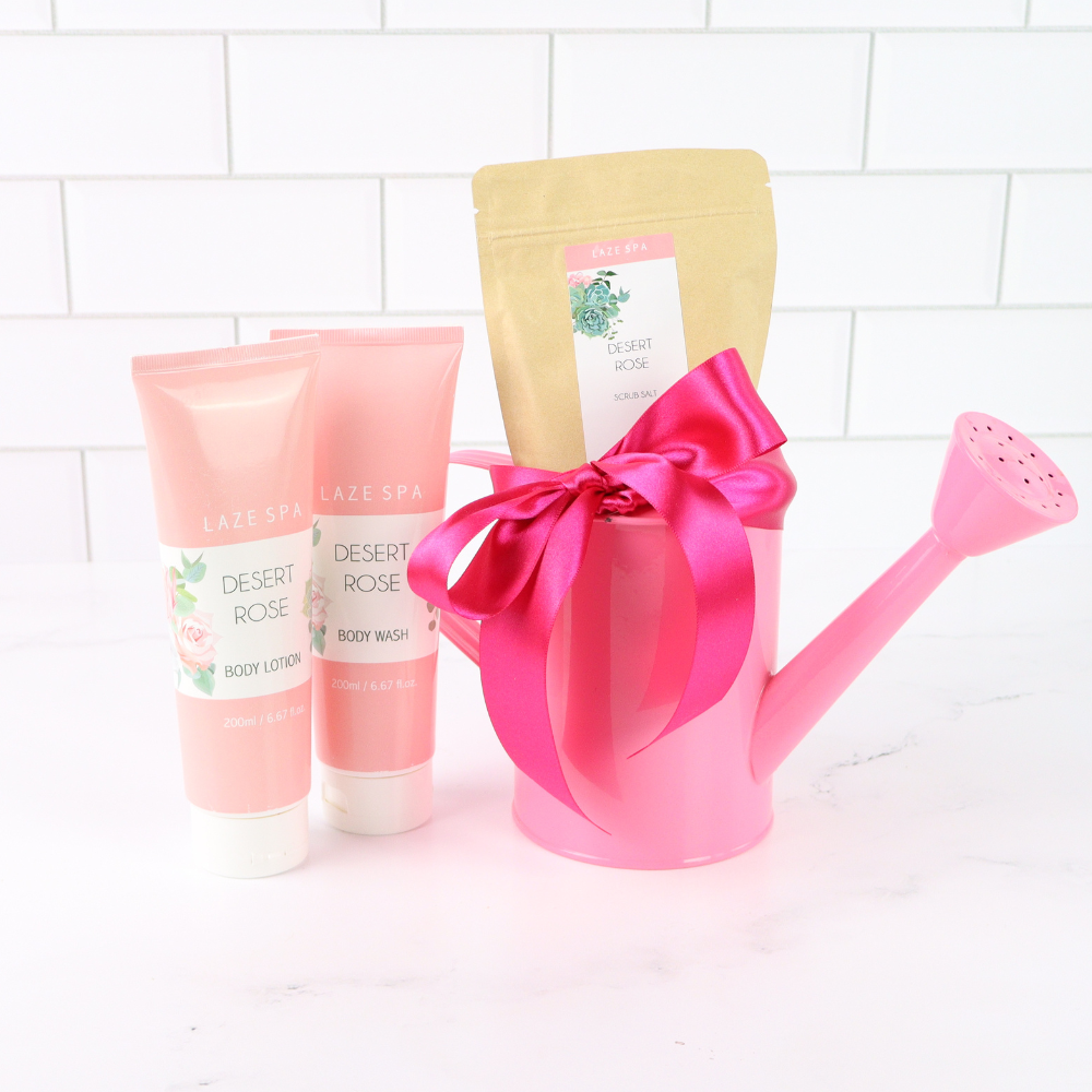 Pink watering can with a bow, body wash, and lotion on a white tiled background