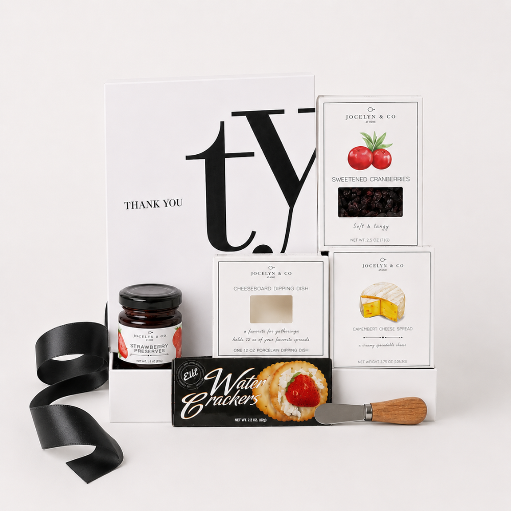 A curated gift box set from Jessica & Co. arranged on a white marble surface, featuring a white 'Thank You' card, a jar of preserves, water crackers, cranberry sauce, cheese spread, a small knife, and a black textured insert inside a gift box.