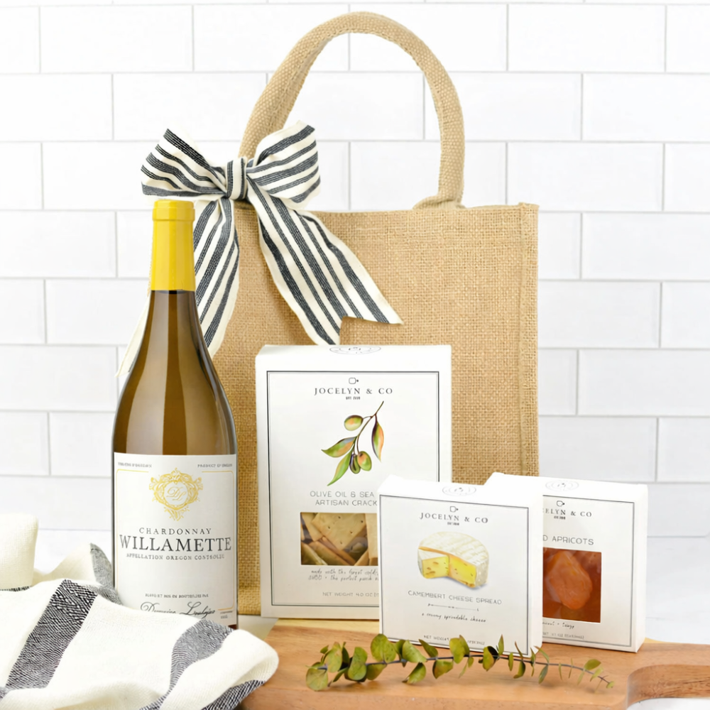 Wine bottle, gift bag with a bow, and cards on a wooden surface with a white tiled background