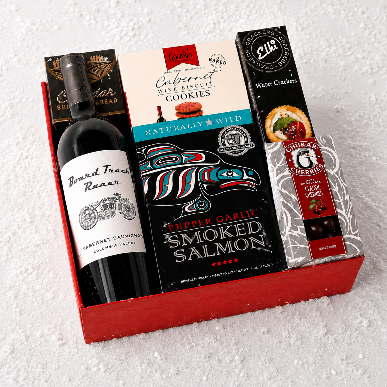 A curated gift box set containing a bottle of Beard Trees Racing Cabernet Sauvignon, a box of Lucky Cabernet Wine Biscuit Cookies, Pepper Garlic Smoked Salmon crackers, and a box of Water Crackers, all arranged in a red gift box on a white textured background.